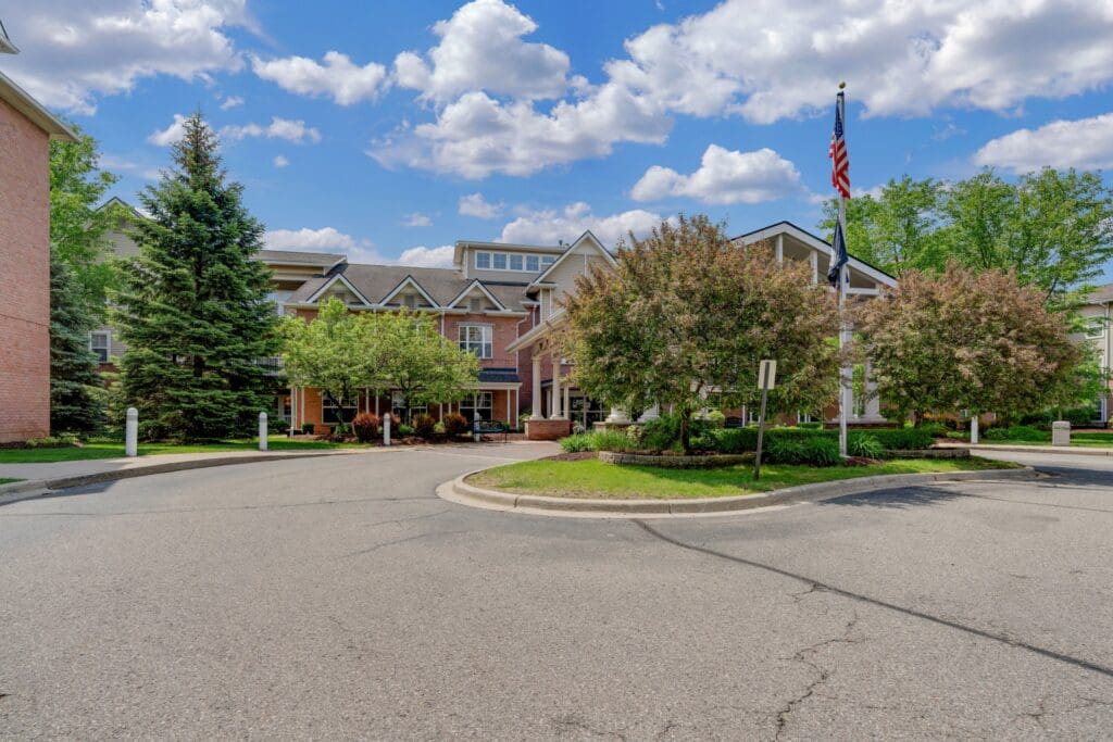Town Village Sterling Heights main building driveway with green trees and an American flag in front of it.