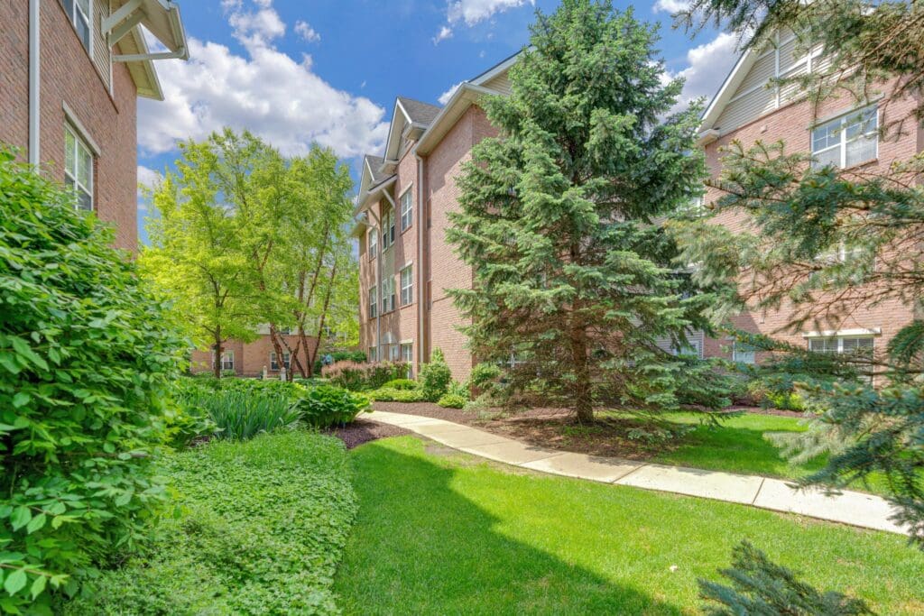 Town Village Sterling Heights senior living community buildings and a walking path between them, as well as a green lawn and trees.