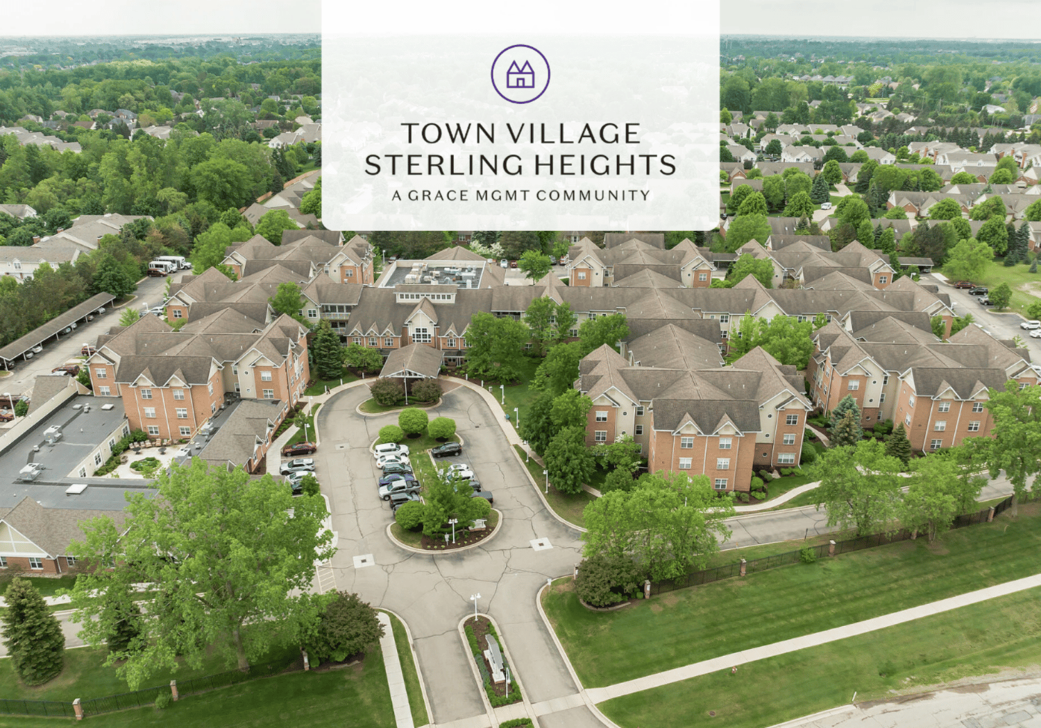 Aerial view of Town Village Sterling Heights apartment community with a circular driveway, cars, and lush green landscaping.