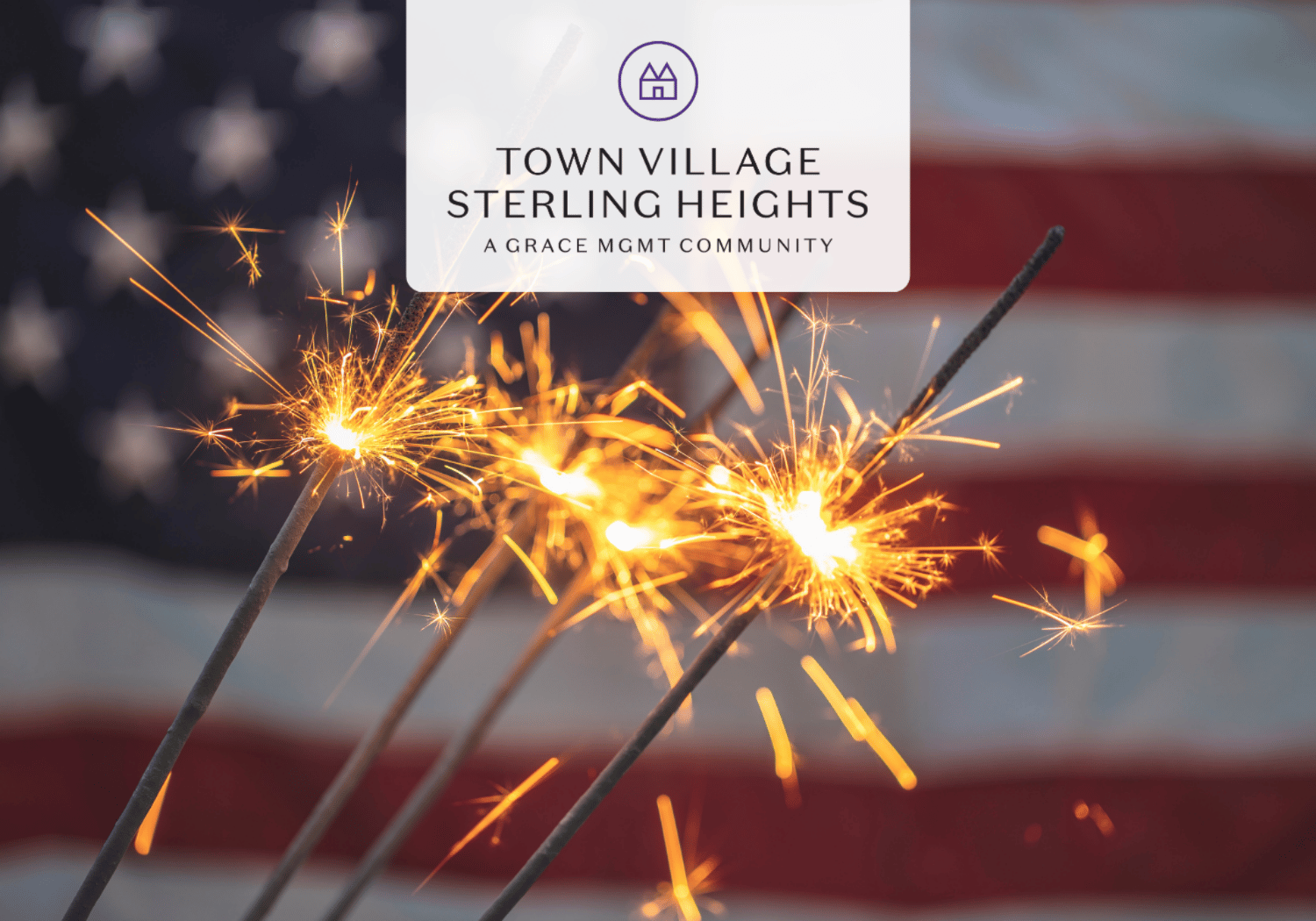 Sparklers explode with orange sparks in the foreground, an American flag blurred in the background, and a white rounded banner at the top center reading 'Town Village Sterling Heights'.